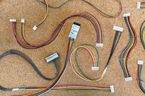 Multi-coloured electronic Faikin cables are pinned to a cork board.