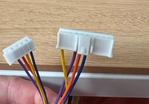 Two white cable connectors with multicolored wires on a wooden surface. Cables connect to a Faikin.